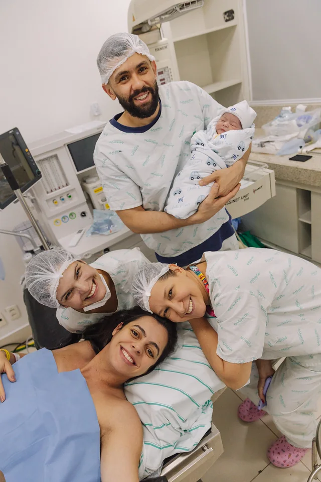 Família e equipe reunidas após o nascimento, com o bebê no colo
